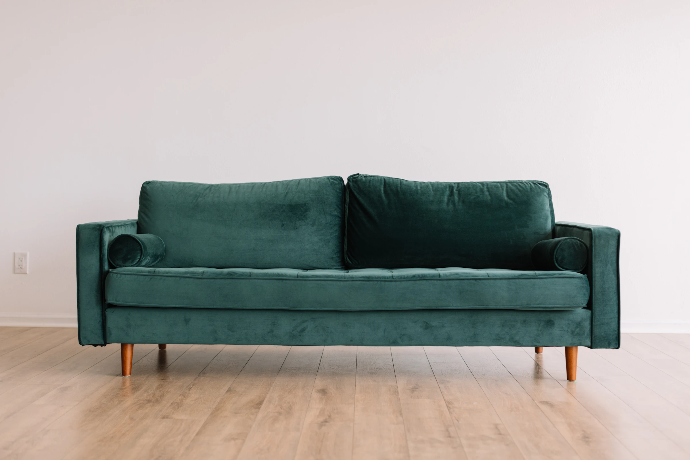 Deep green velvet sofa with tapered wooden legs against a white wall