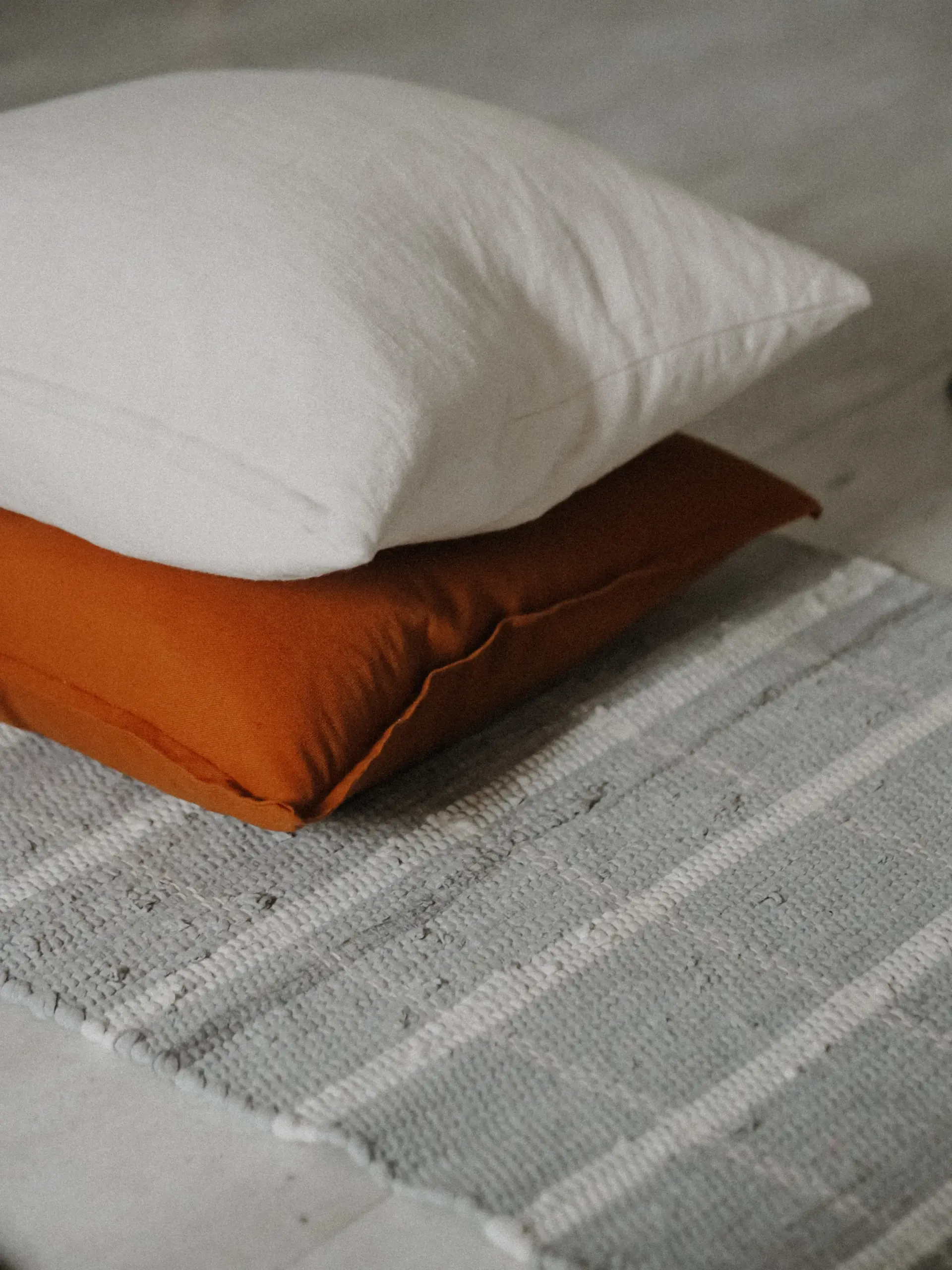 White linen cushion resting on a rust cushion on a striped throw