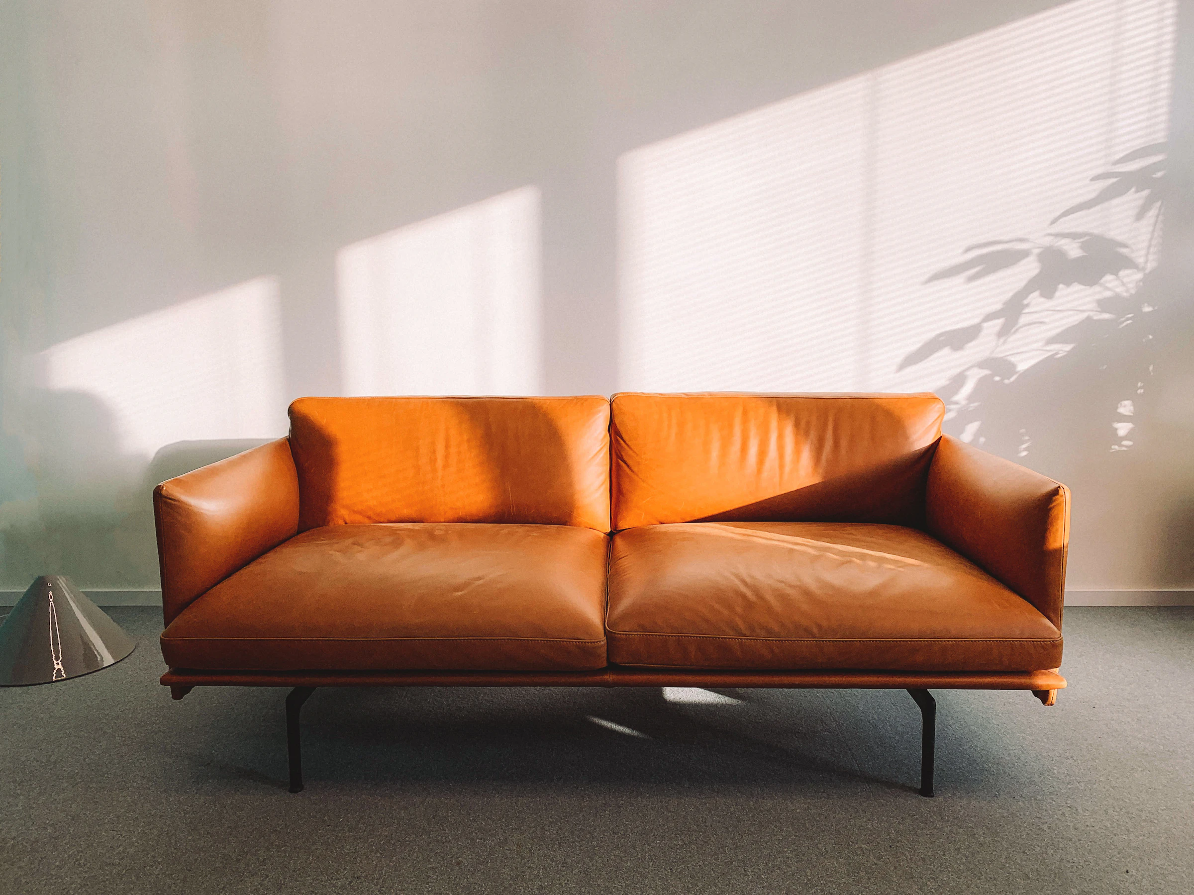 Cognac leather three-seat sofa with slim black metal legs in a sunlit room