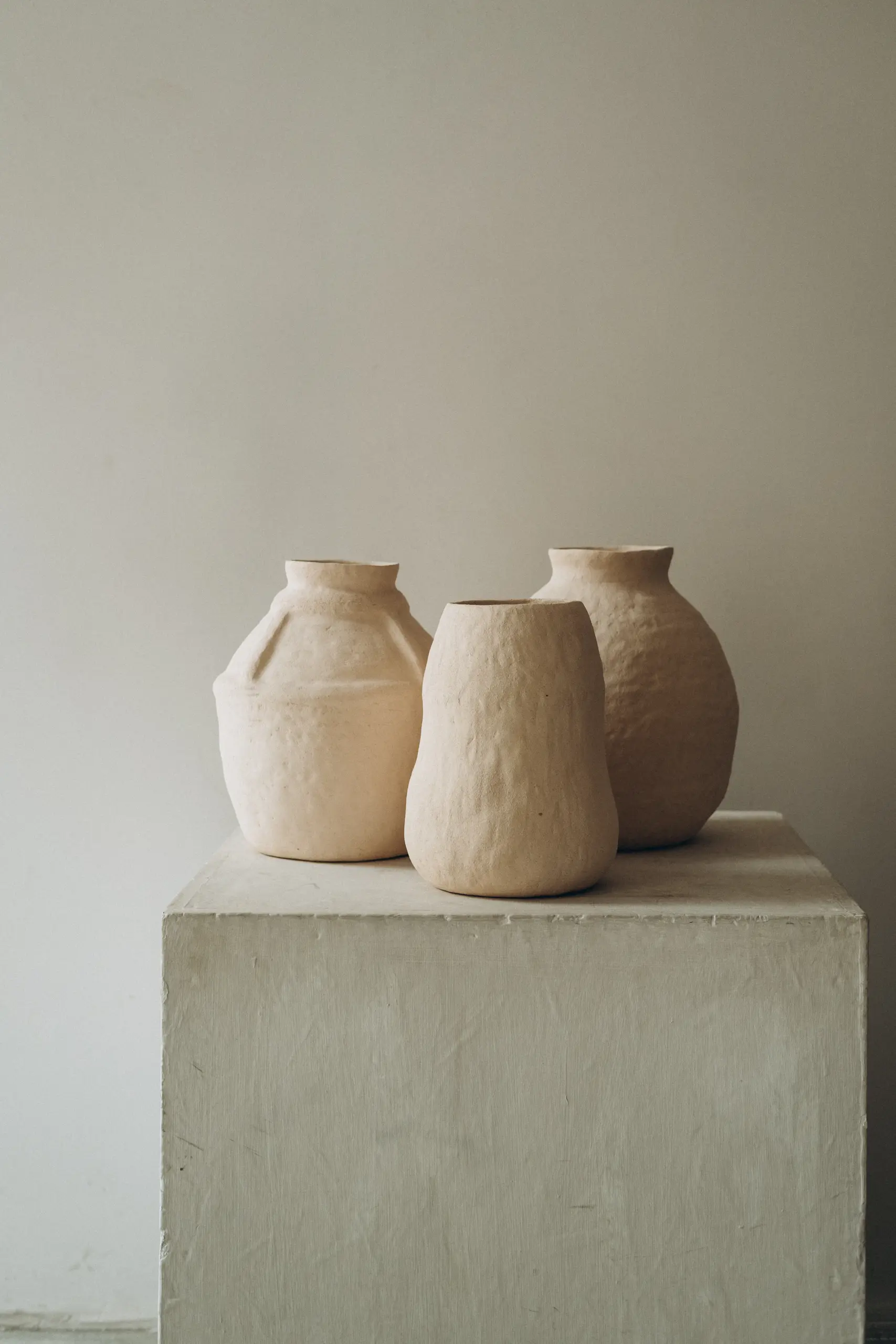 Three unglazed clay vases of different heights on a concrete plinth